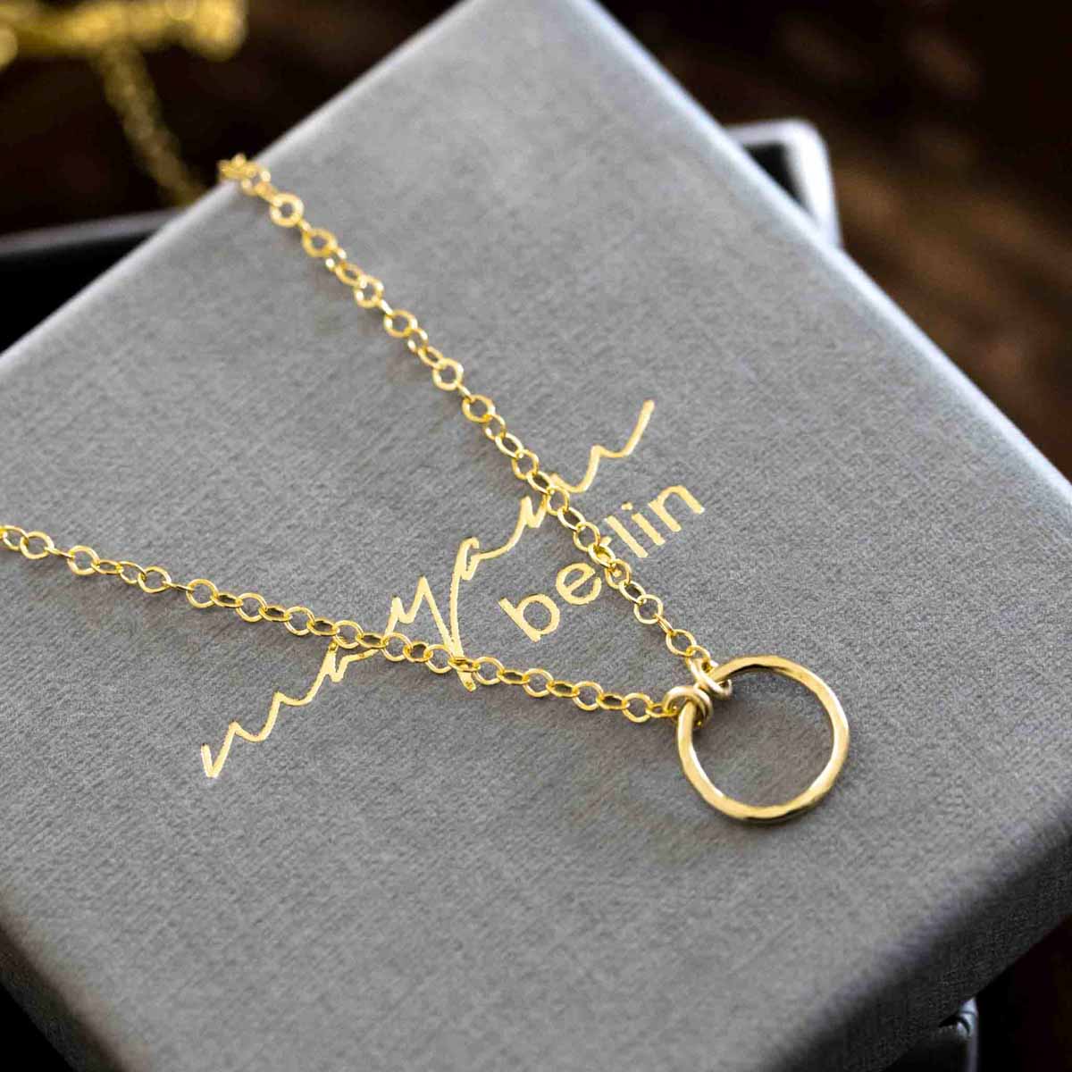 Eine feine Goldkette mit offenem Ring-Anhänger liegt auf einem grauen Schmucketui.