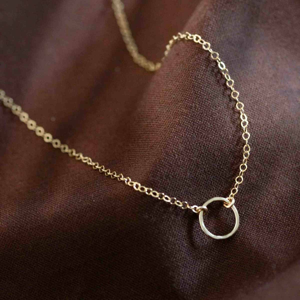 Eine feine Goldkette mit einem offenen Ring in der Mitte auf braunem Hintergrund.