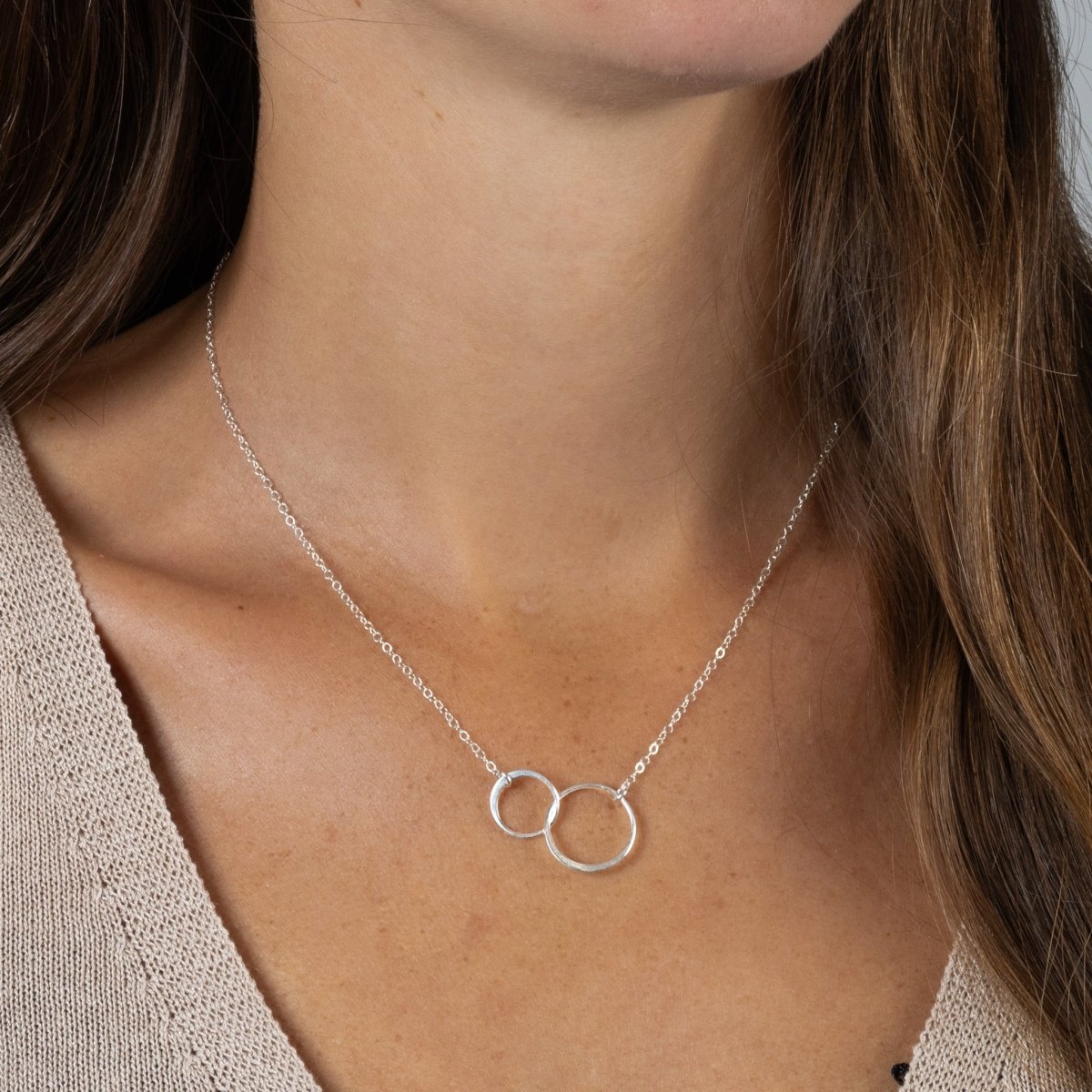 Eine zierliche 925 Silberkette mit zwei miteinander verschlungenen und unterschiedlich großen Ringen in der Mitte hängt vom Hals des Models.