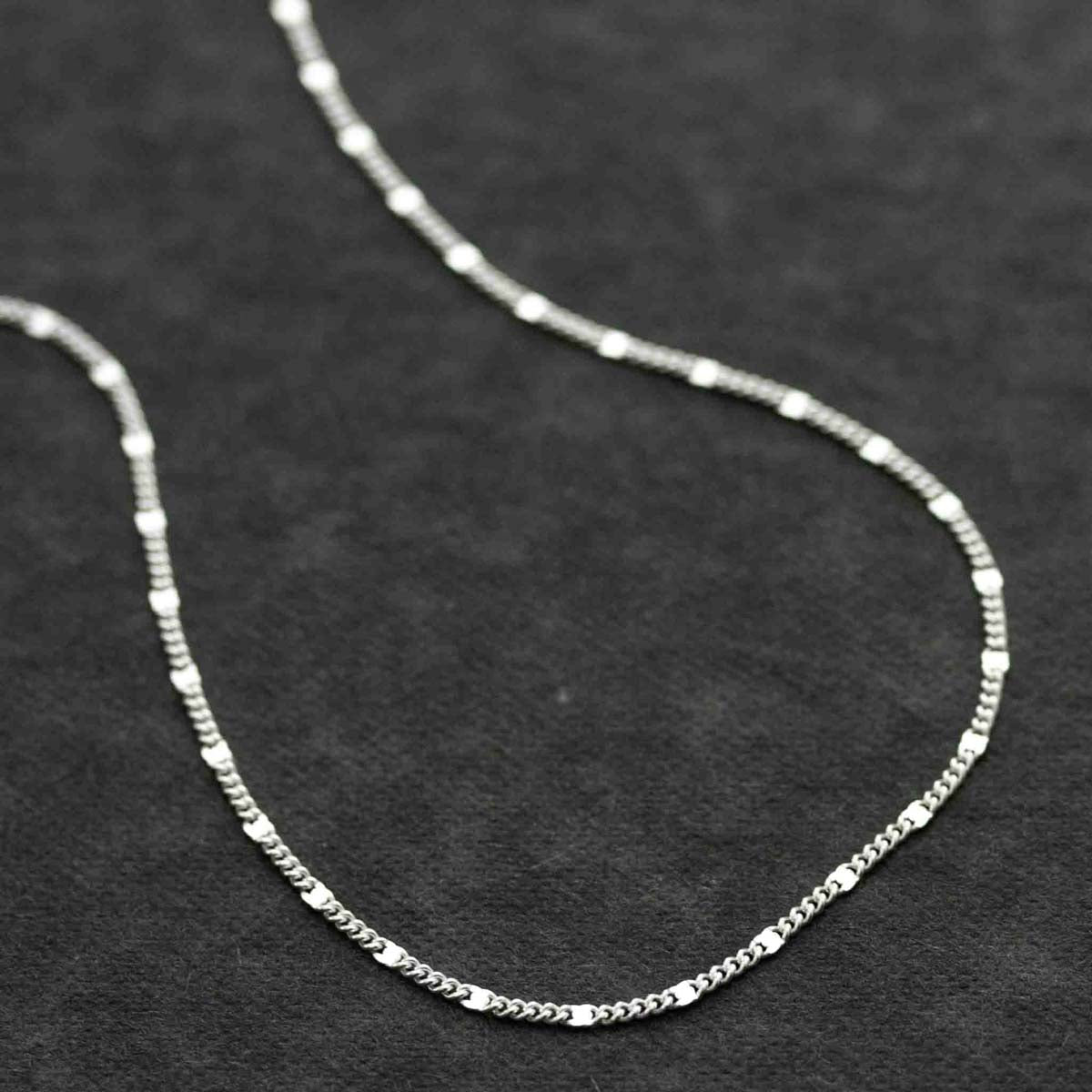 Eine feine Halskette aus 925 Silber liegt auf dunklem Hintergrund.