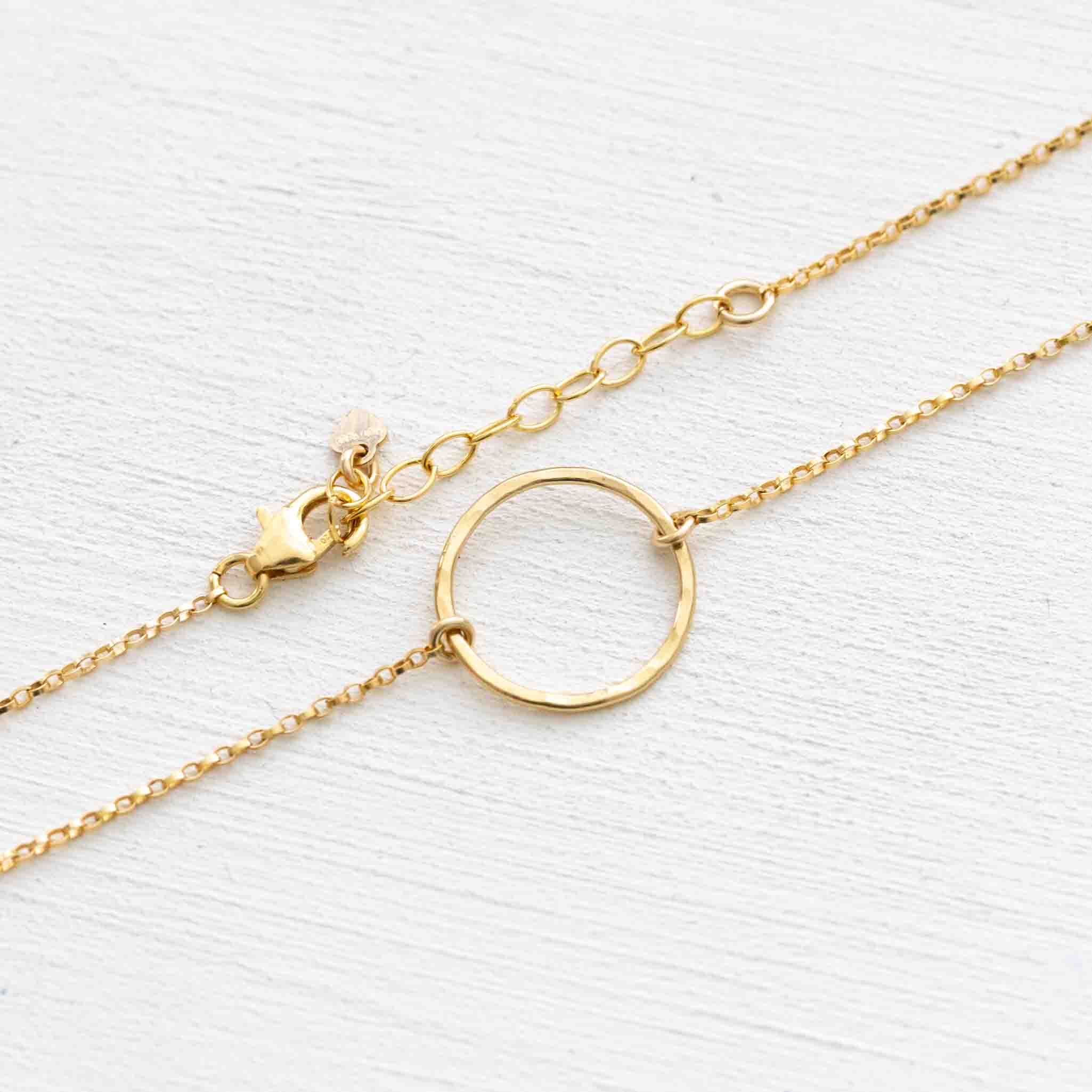 Ein goldenes Fußkettchen mit einem offenen Ring in der Mitte liegt auf weißem Hintergrund.
