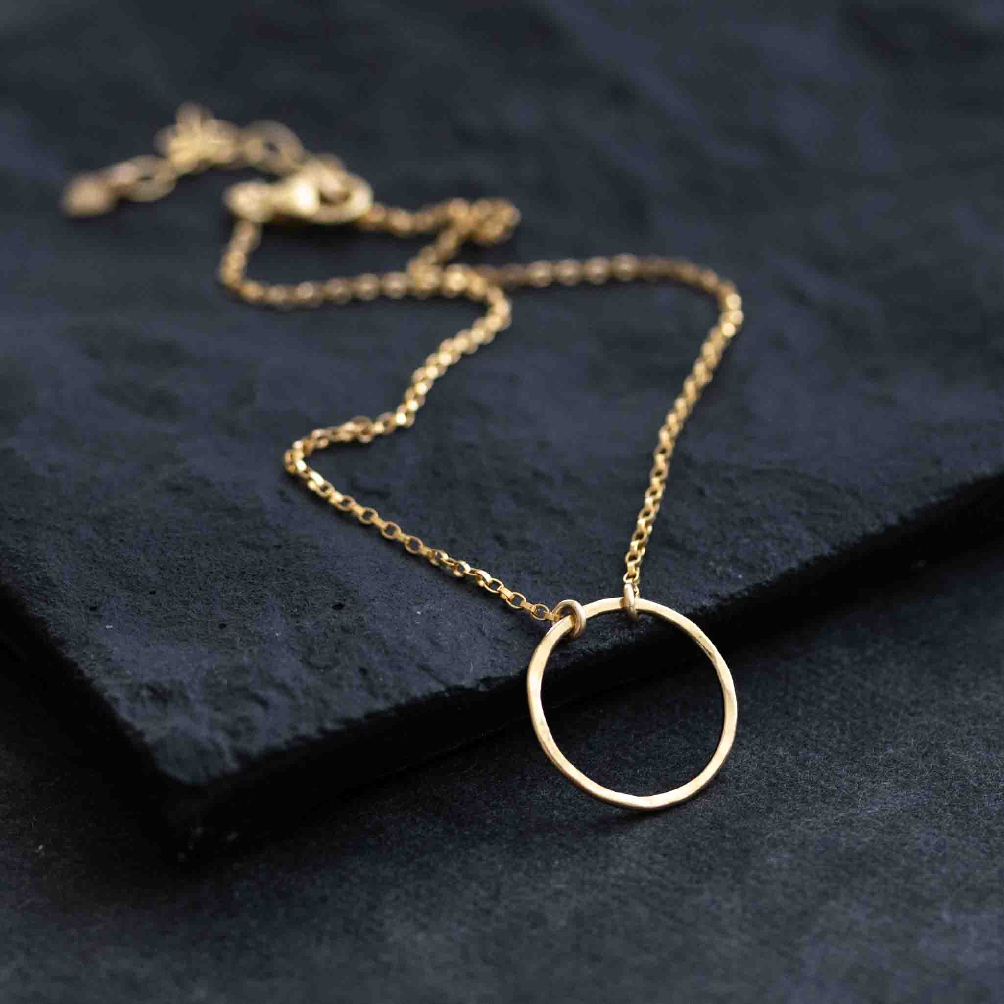 Ein goldenes Fußkettchen mit einem Ring in der Mitte liegt auf schwarzem Hintergrund.