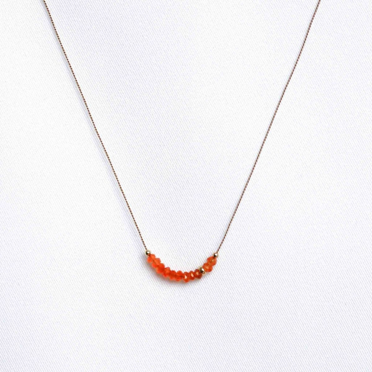 Feine Seidenkette mit orangen Karneol-Rondellen auf weißem Hintergrund.