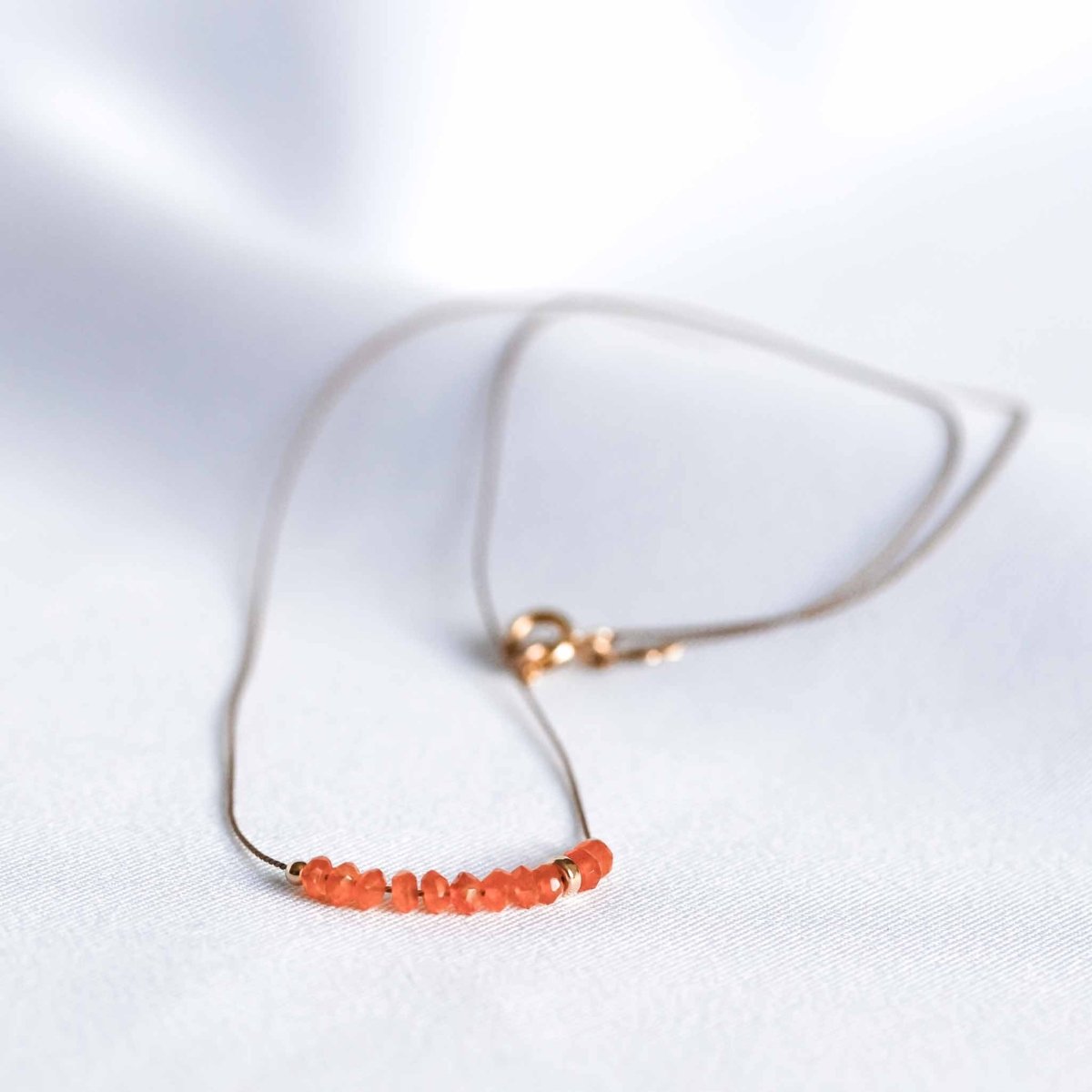 Feine Seidenkette mit orangen Karneol-Rondellen auf weißem Hintergrund.
