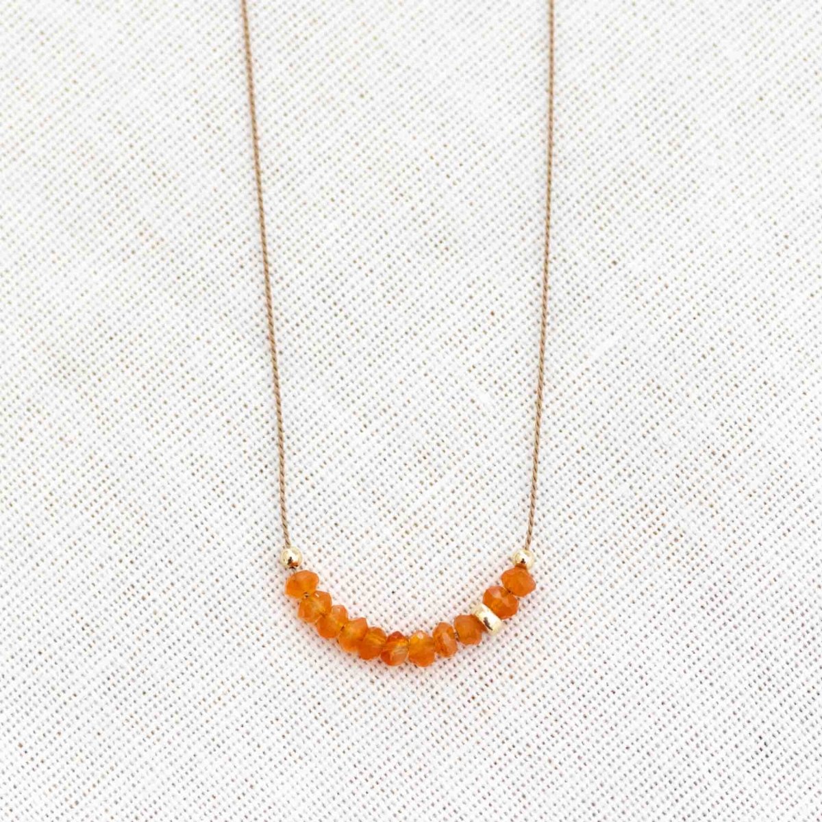 Feine Seidenkette mit orangen Karneol-Rondellen auf weißem Hintergrund.