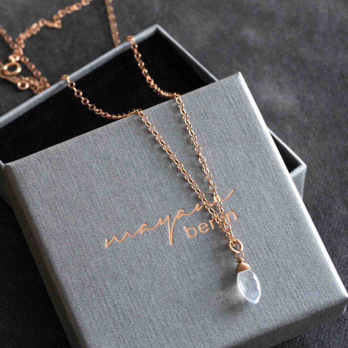 Eine Rosé Goldfill-Kette mit einem spitz zulaufenden Mondstein-Anhänger liegt auf einem geöffneten, grauen Kartonetui.