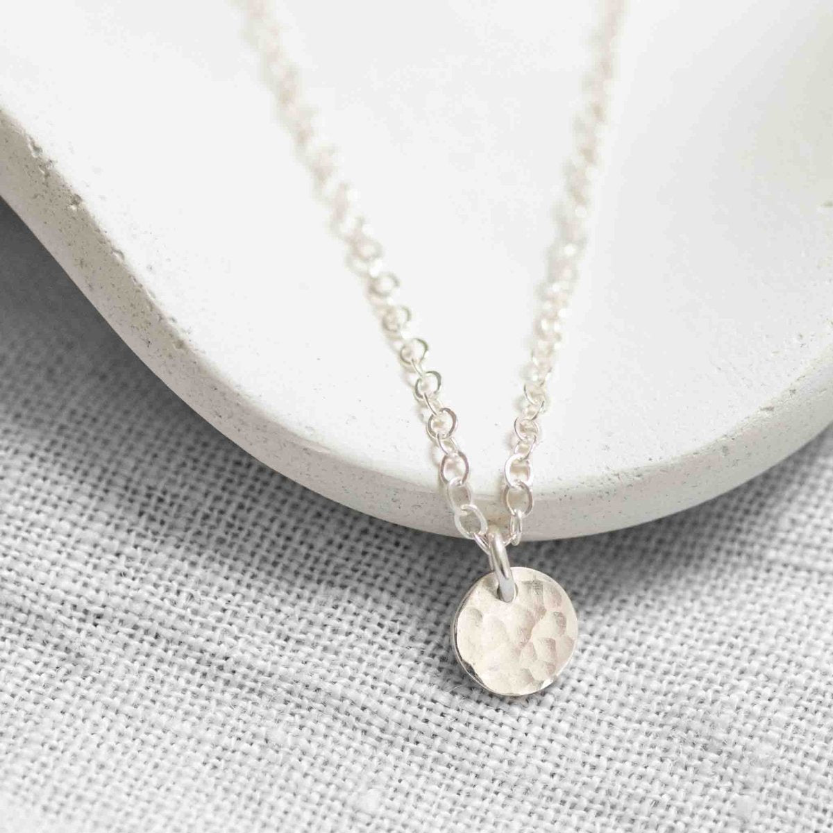 Detailansicht des gehämmerten Plättchens an einer feinen Ankerkette aus 925 Silber vor weißem Hintergrund.