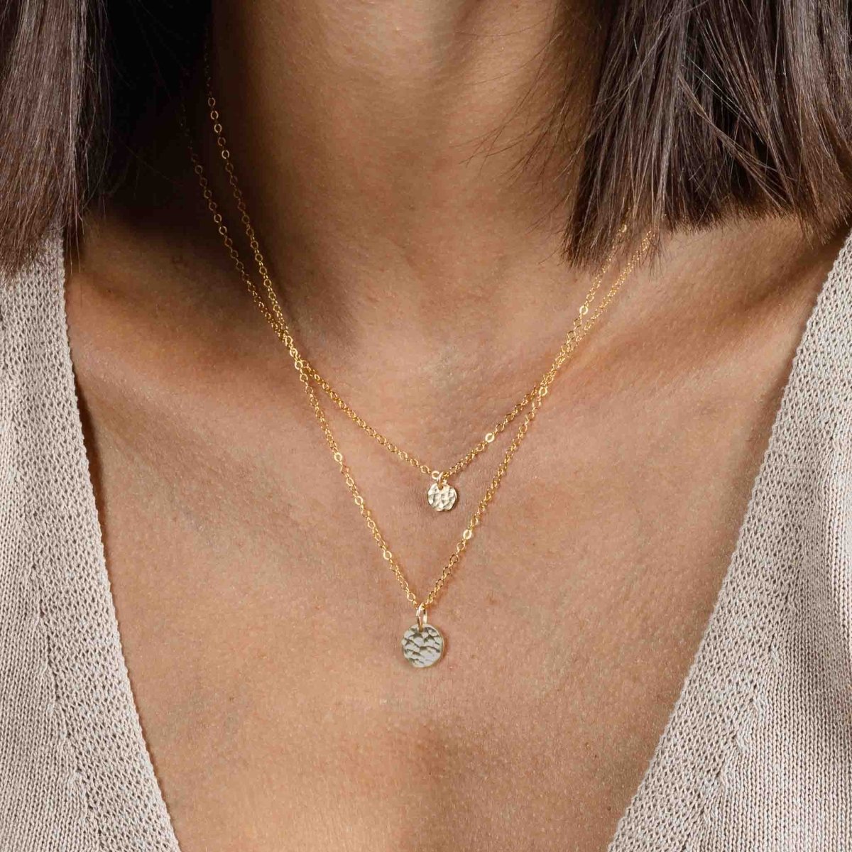 Am Hals des Models hängen zwei Goldketten mit gehämmerten Plättchenanhängern: ein kleineres Plättchen an der kürzeren Kette und ein größeres an der längeren Kette.