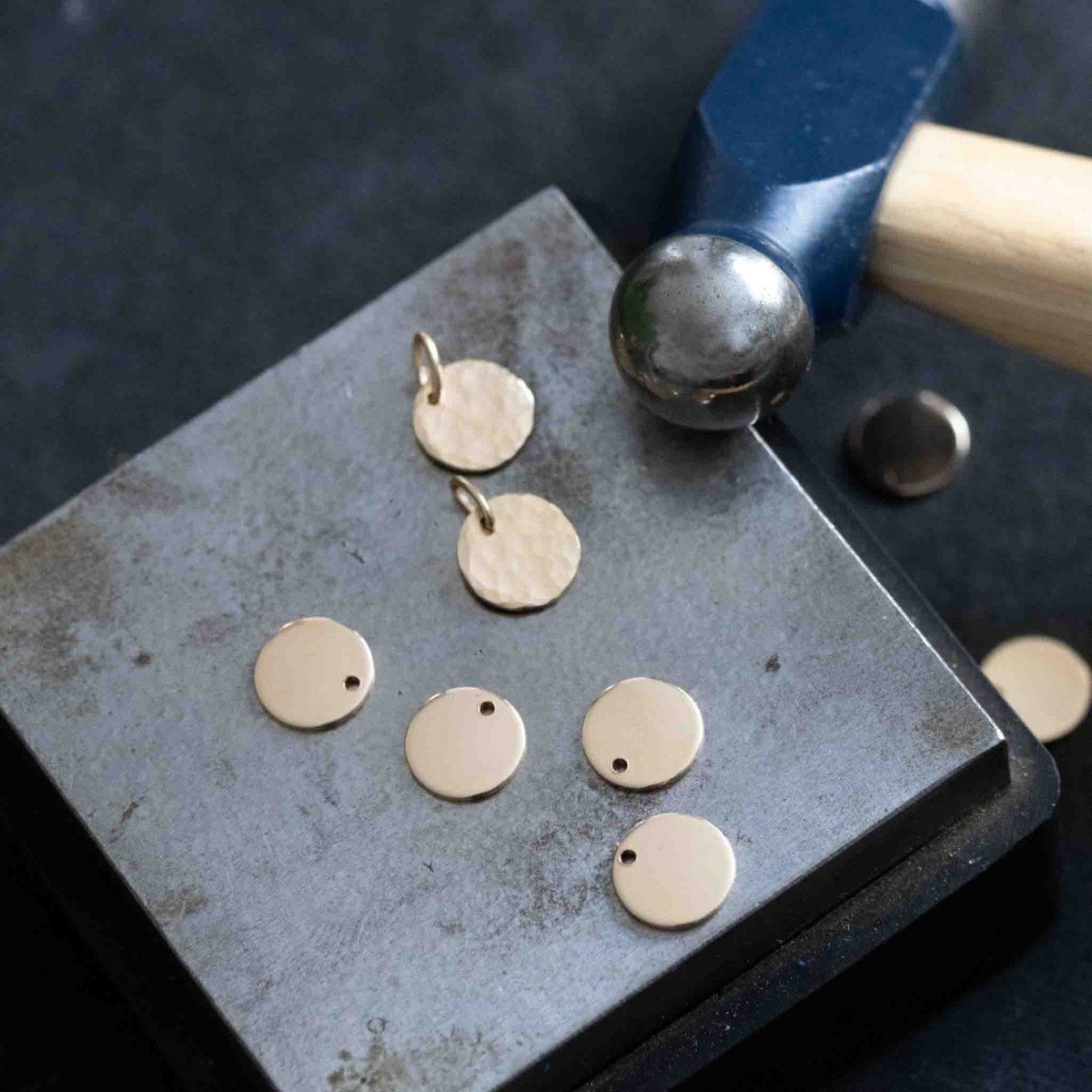 Ein Stempelblock mit gehämmerten und ungehämmerten runden, goldenen Plättchen, daneben ein Schmuckhammer.