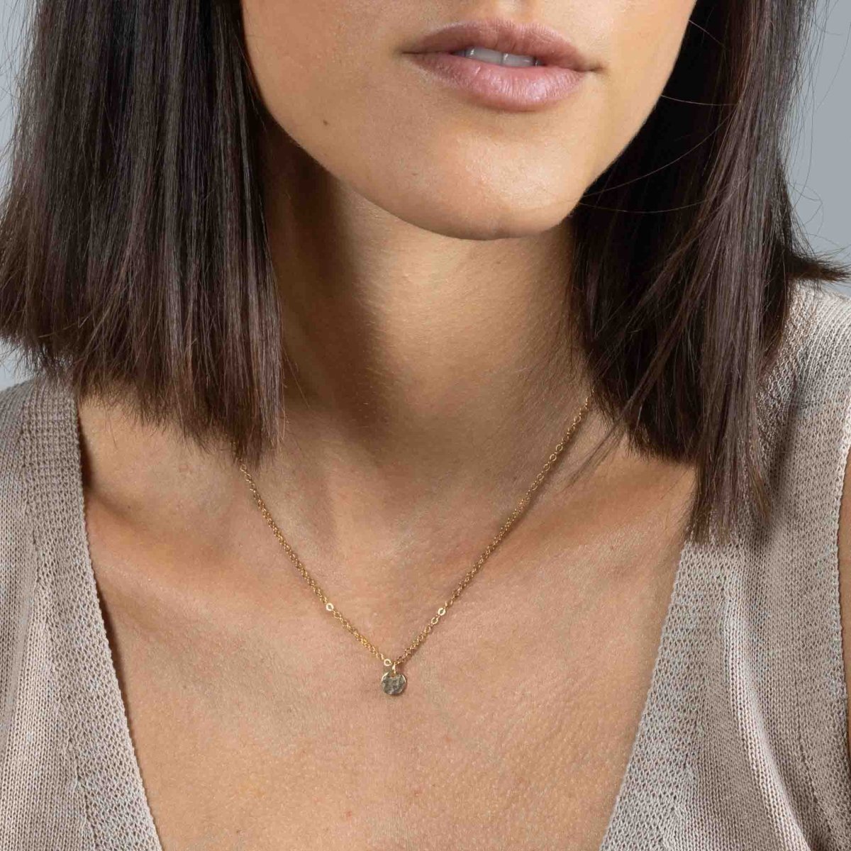 Eine dünne Roségold Halskette mit einem kleinen, gehämmerten Plättchen-Anhänger hängt vom Hals des Models.