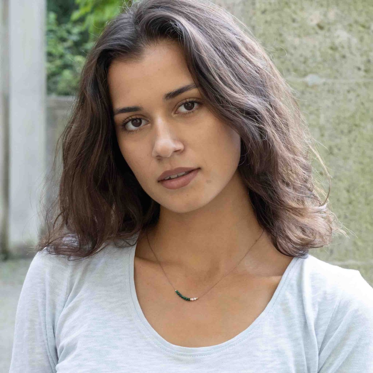 Dünne, beige Seidenkette mit aufgezogenen Malachit- und Süßwasserperlen, sowie goldenen Akzenten am Hals des Models.