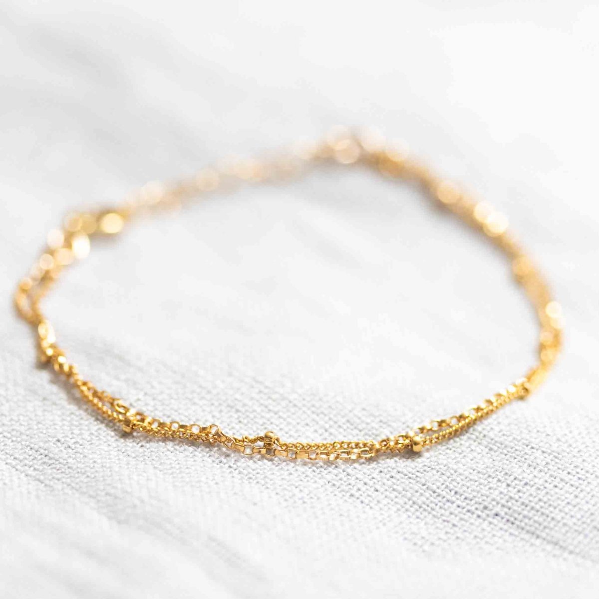 Auf weißem Hintergrund liegt ein zierliches, doppelt gelegtes Armband aus Satellitenkette und Rolokette, beide in gold.