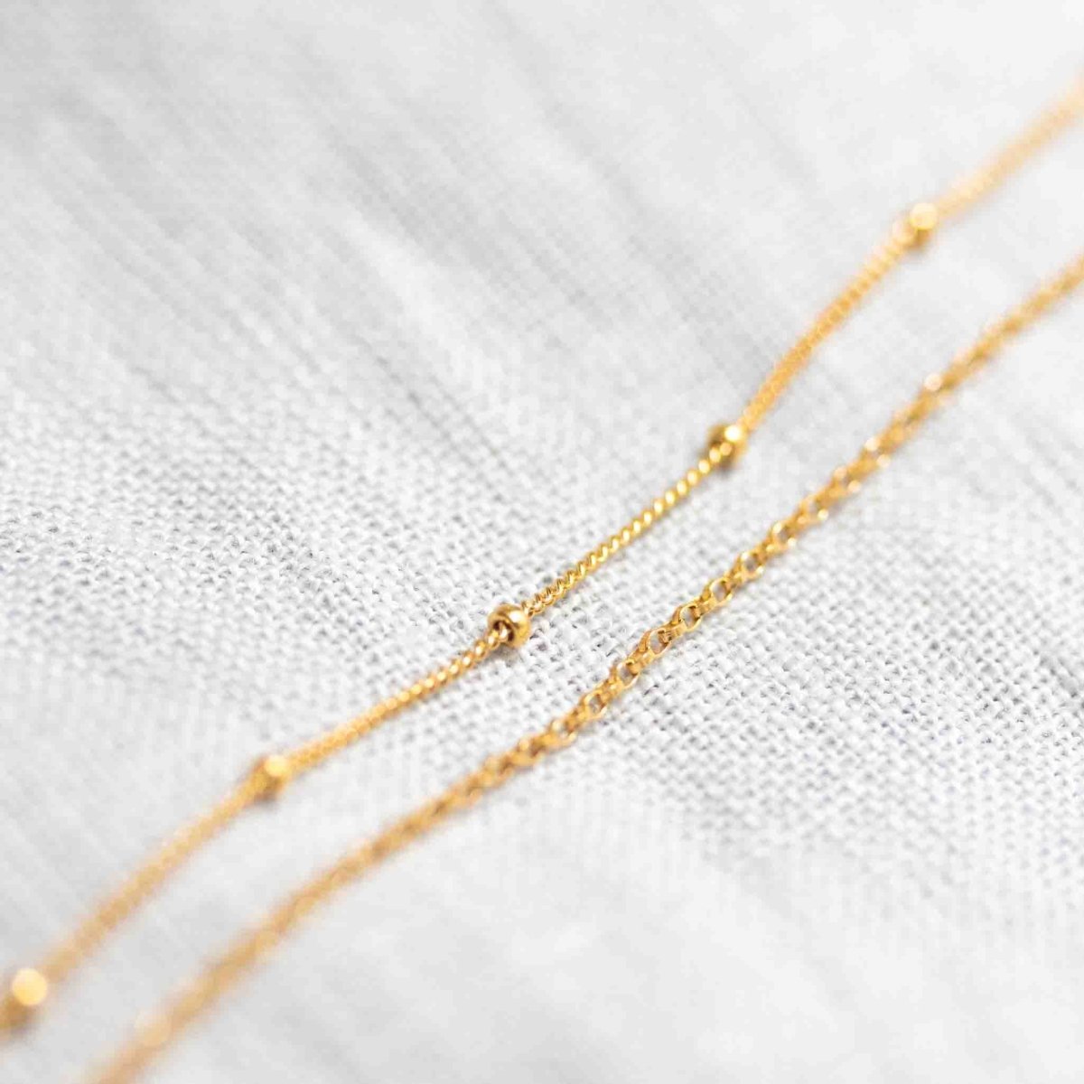 Auf weißem Hintergrund liegt ein zierliches, doppelt gelegtes Armband aus Satellitenkette und Rolokette, beide in gold.