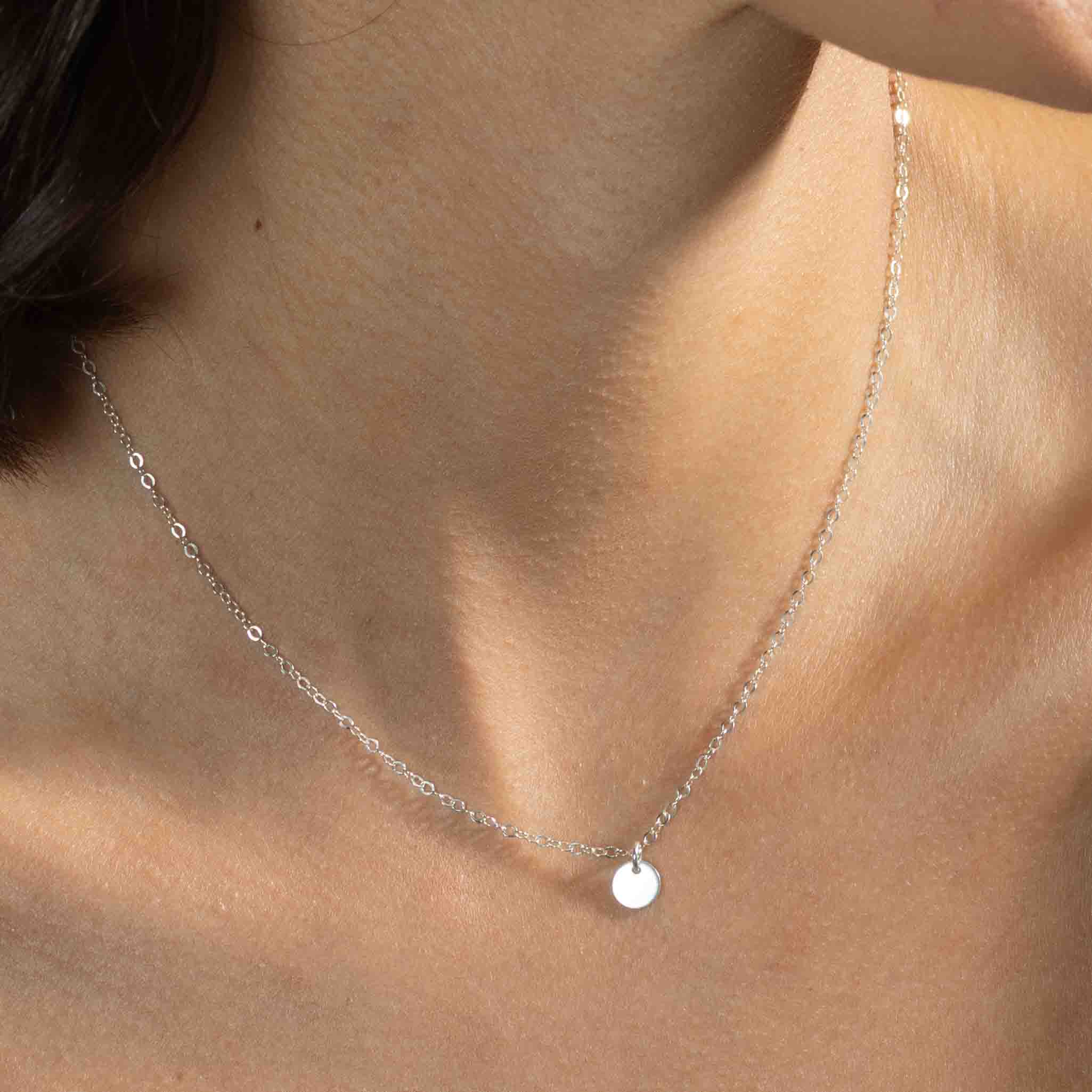 Am Hals des Models hängt eine kurze, feine Ankerkette aus 925 Silber mit einem kleinen, runden Plättchenanhänger, der silbern glänzt.