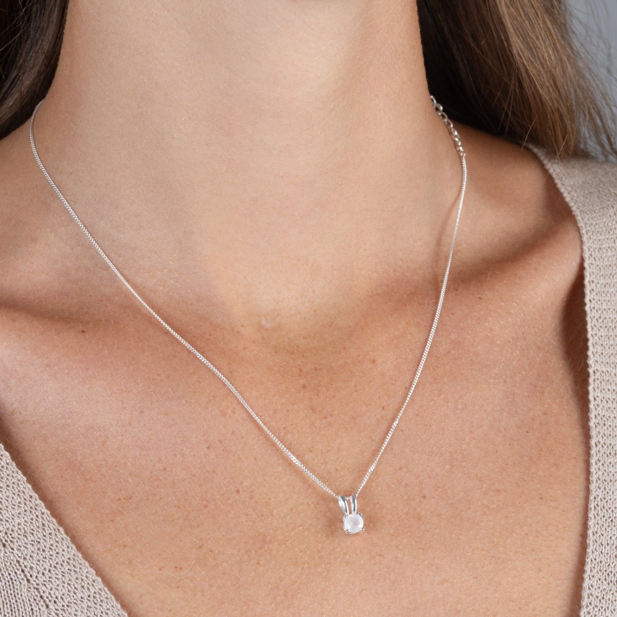 Eine feine, silberne Panzerkette mit einem winzigen, runden, in Silber gefassten Mondstein Anhänger hängt am Hals des Models.