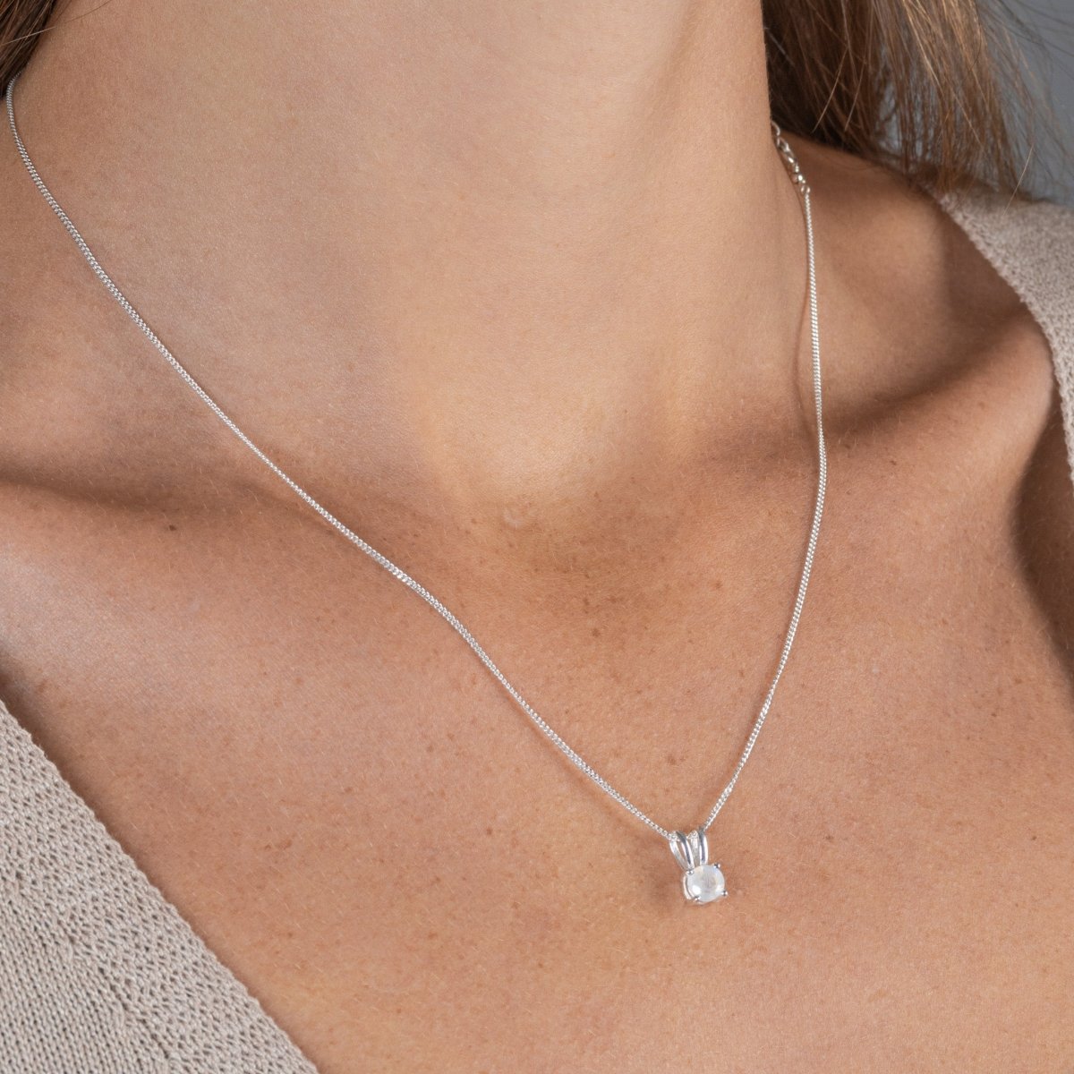 Eine feine, silberne Panzerkette mit einem winzigen, runden, in Silber gefassten Mondstein Anhänger hängt am Hals des Models.