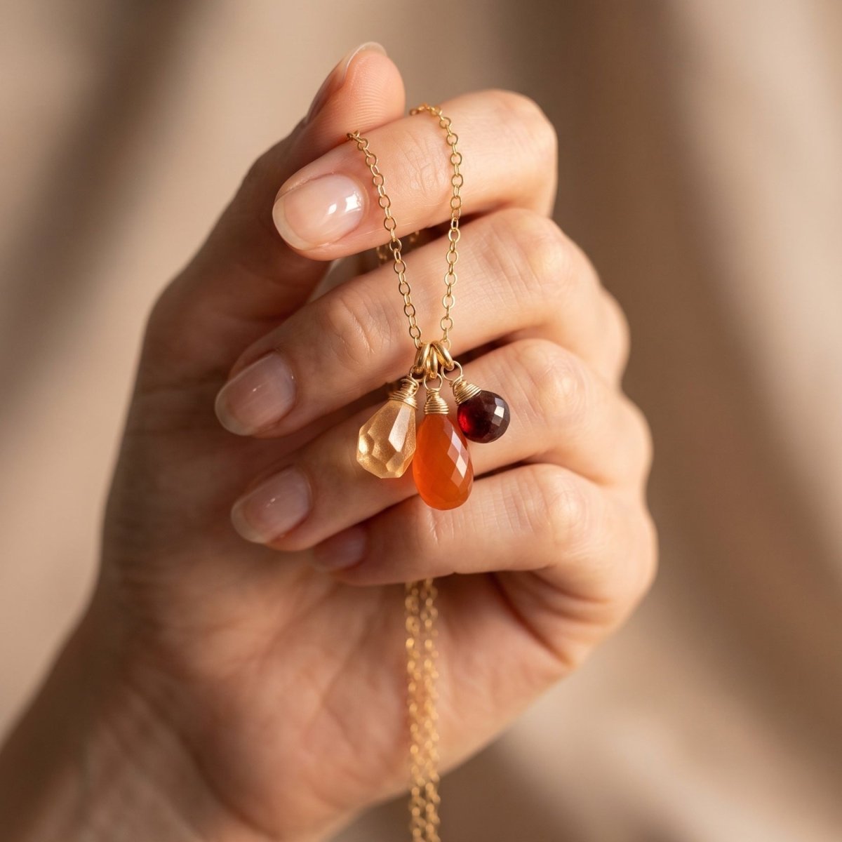 Zierliche Goldkette mit Citrin-, Karneol- und Granat-Anhänger vor Hand hängend.