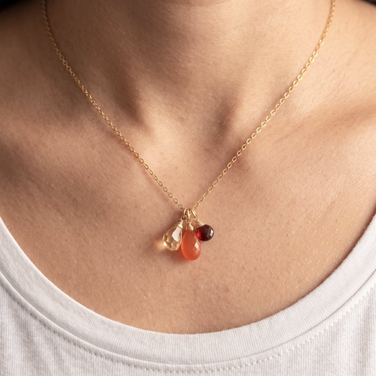 Zierliche Goldkette mit Citrin-, Karneol- und Granat-Anhänger am Hals getragen.