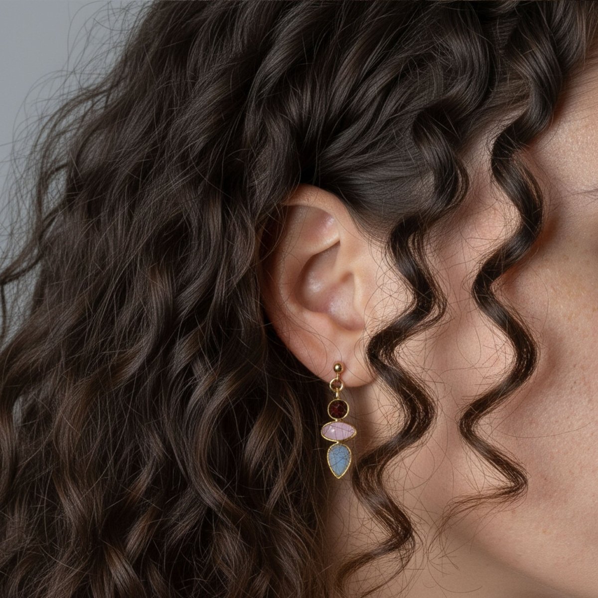 Ein goldener Multi-Edelstein-Ohrstecker, bestehend aus Granat, rosa Chalcedon und Mondstein, hängt am Ohr des Models.