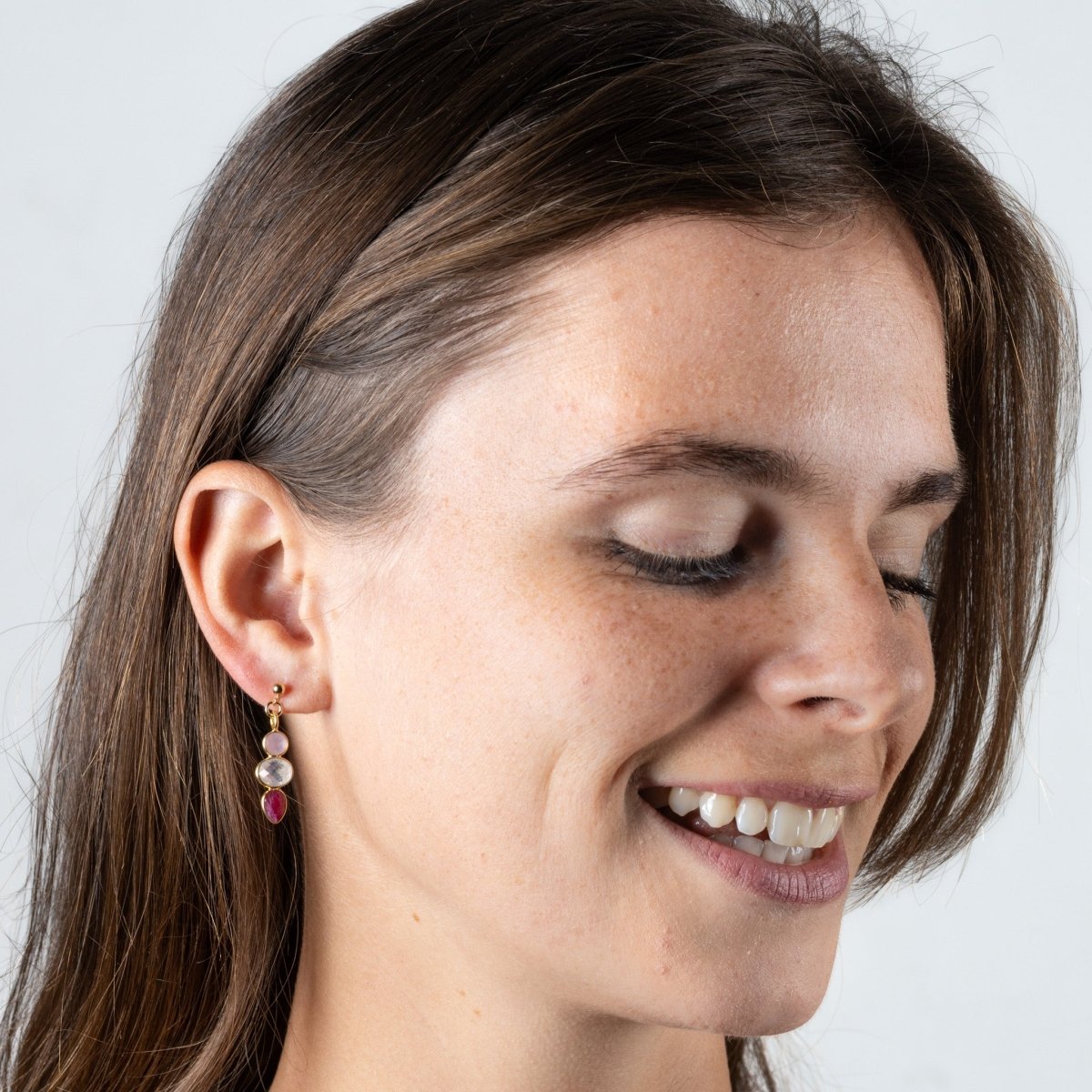 Ein goldener Ohrstecker mit einem rosa Chalcedon, einem Mondstein und einem Rubin hängt am Ohr des Models.