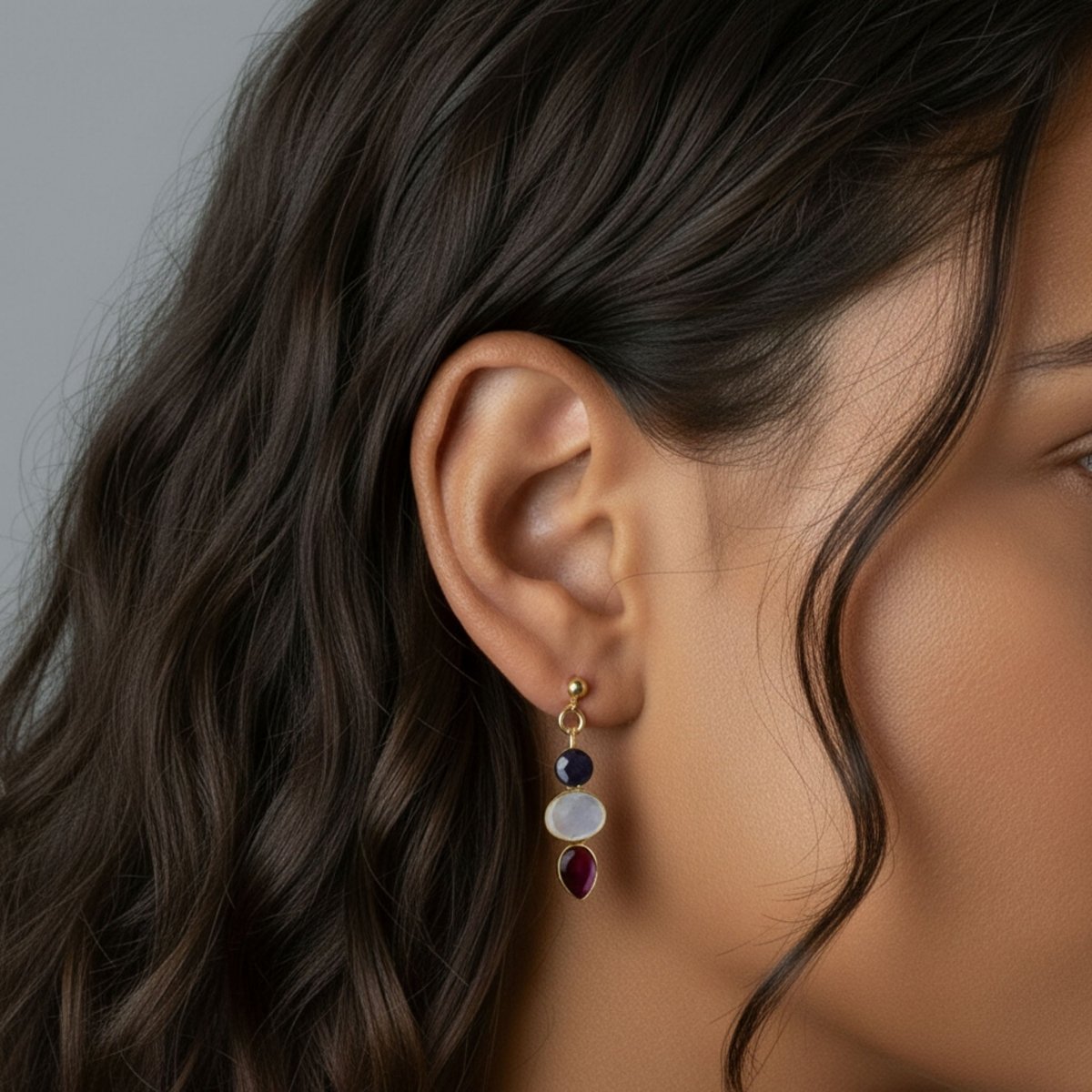 Ein Multi-Edelstein Ohrring mit Saphir, Mondstein und Rubin in gold gefasst hängt am Ohr des Models.