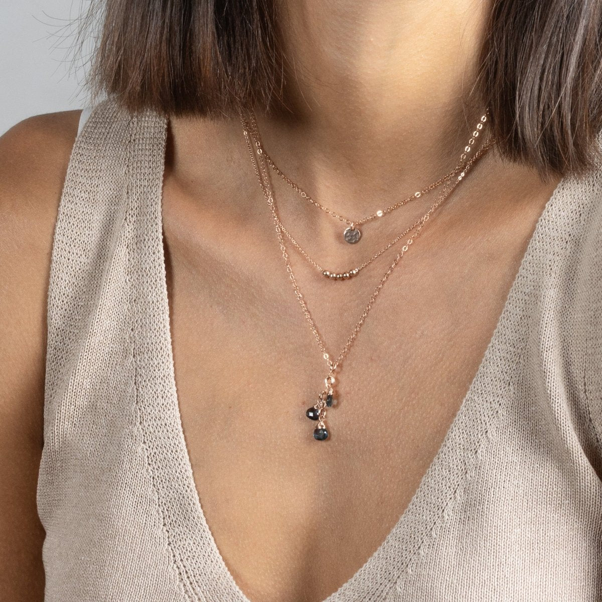 Am Hals des Models hängen drei unterschiedlich lange Roségold-Ketten. An der kürzesten hängt ein kleines, gehämmertes Plättchen und an der längsten baumeln drei London Blautopas-Tropfen.