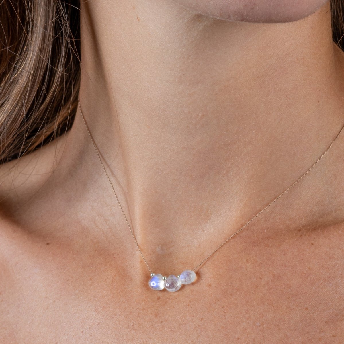 Eine dünne Seidenkette mit drei aufgezogenen Mondsteinen hängt am Hals des Models.