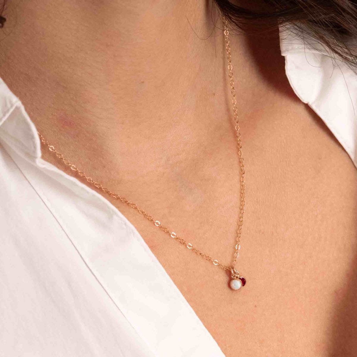 Eine zierliche Goldkette mit zwei winzigen, runden Anhängern, einem Opal und einem Granat, am Hals des Models.