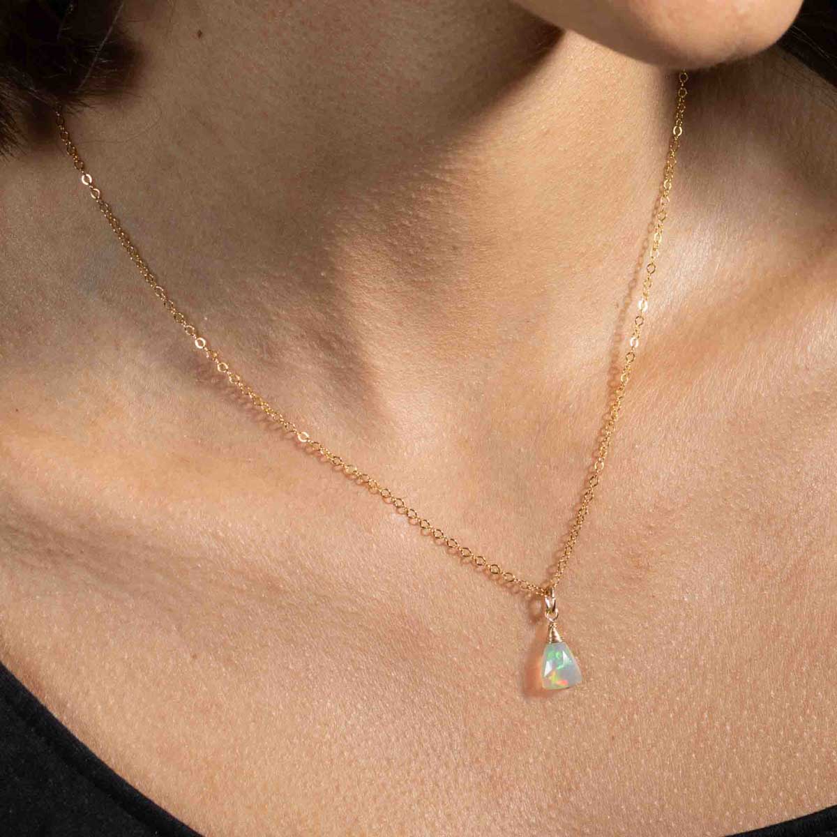 Eine zierliche Goldkette mit einem dreieckigen Welo Opal-Anhänger hängt am Hals des Models.