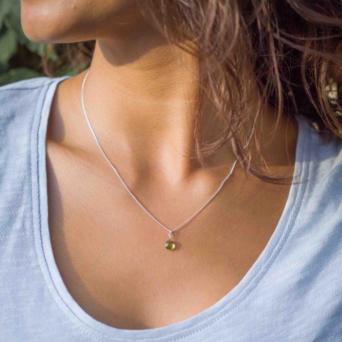 Am Hals des Models hängt eine kurze Silberkette mit einem kleinen, grünen Peridot-Anhänger.