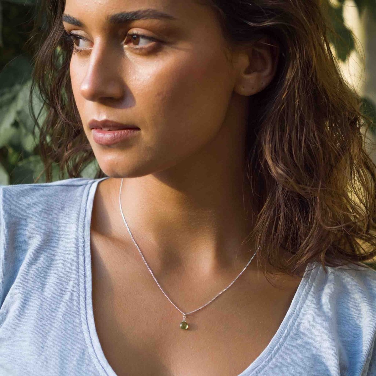 Am Hals des Models hängt eine kurze Silberkette mit einem kleinen, grünen Peridot-Anhänger.