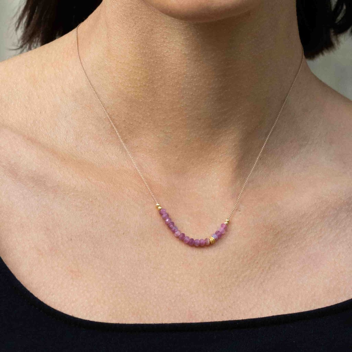 Am Hals des Models hängt eine dünne Seidenkette mit einer Reihe rosa Turmalin-Rondellen und goldenen Akzenten in der Mitte.