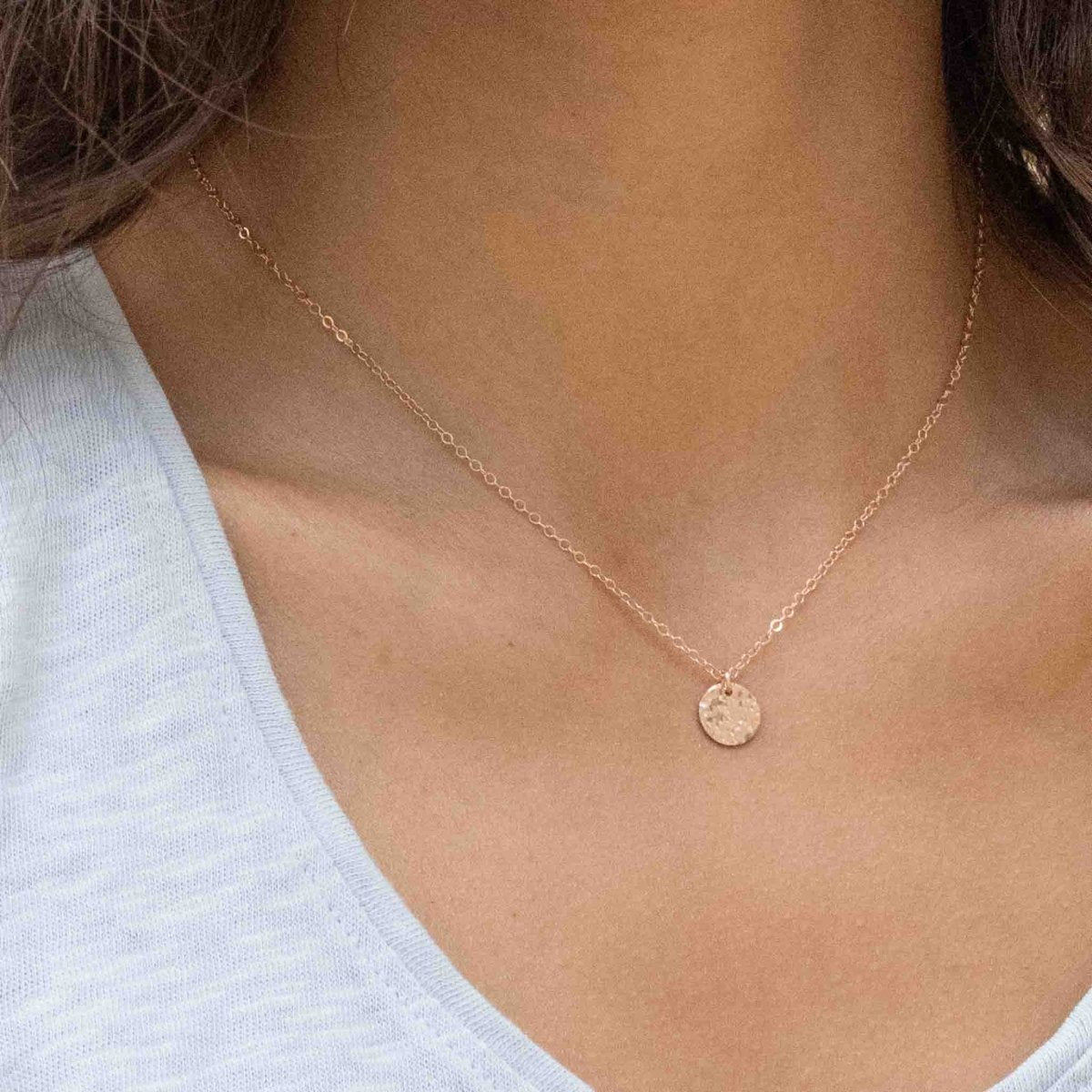 Nahaufnahme einer rosé goldenen Ankerkette mit einem runden, gehämmerten Plättchen am Hals des Models