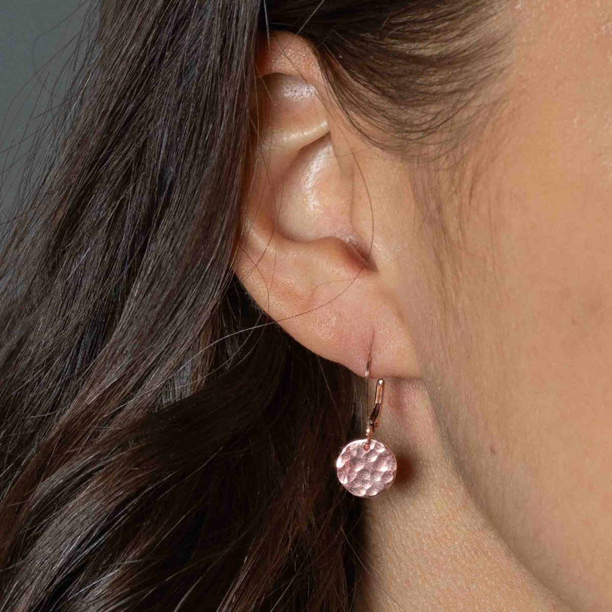 Am Ohr des Models hängt ein rose goldener Ohrring mit einem gehämmerten Plättchen.