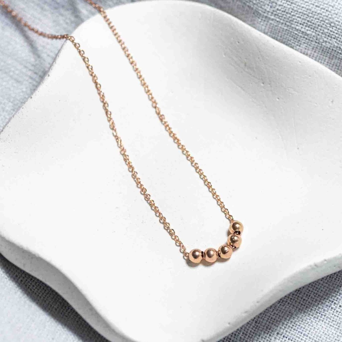 Eine feine Rosé Goldfill-Kette mit fünf kleinen Rosegold-Perlen auf weißem Hintergrund.