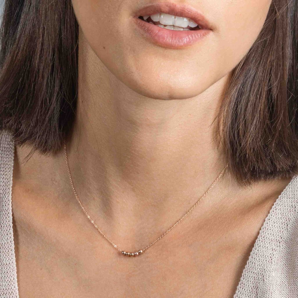 Am Hals des Models hängt eine kurze Roségold-Kette mit fünf aufgezogenen kleinen Rosegold-Perlen in der Mitte.
