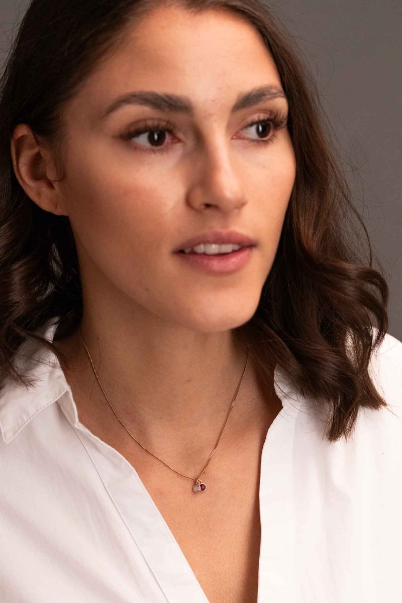 Eine rosé goldene Halskette mit einem winzigen Opal und einem winzigen Rubin-Anhänger am Hals des Models.