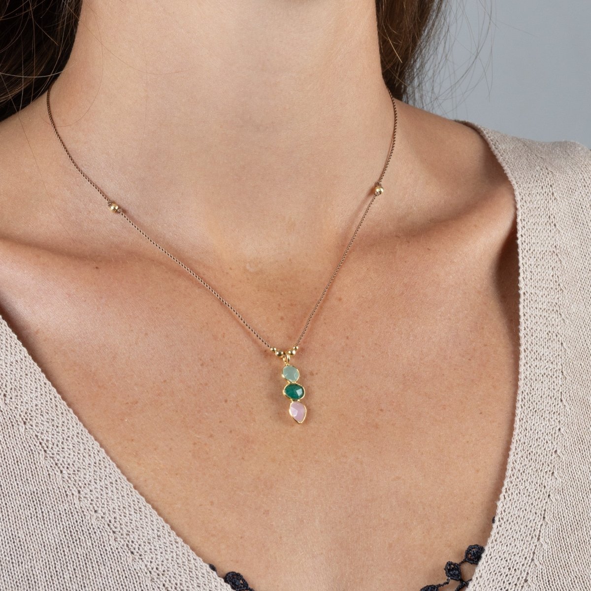 Eine kurze Schnurkette mit einem bunten Multi-Edelsteinanhänger und goldenen Zierelementen hängt am Hals des Models.