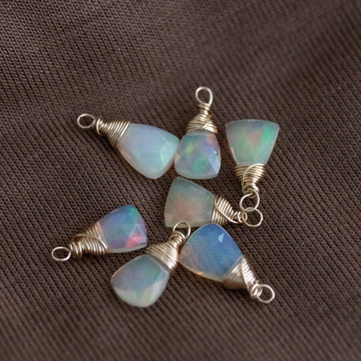 Mehrere dreieckige Opal-Anhänger mit goldener Drahtumwicklung liegen auf braunem Untergrund.