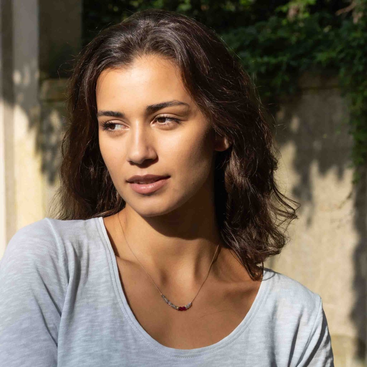 Eine Halskette aus beigem Seidenband, auf das einige Labradorit- und rote Achat-Rondelle aufgezogen sind, am Hals des Models.