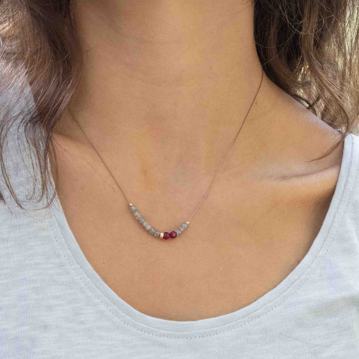 Eine Halskette aus beigem Seidenband, auf das einige Labradorit- und rote Achat-Rondelle aufgezogen sind, am Hals des Models.