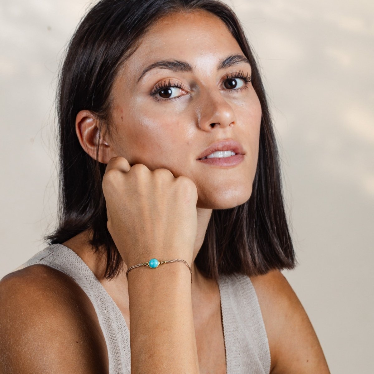 Das Model trägt ein beiges Seidenarmband am Handgelenk, in dessen Zentrum ein runder Türkis eingearbeitet ist.