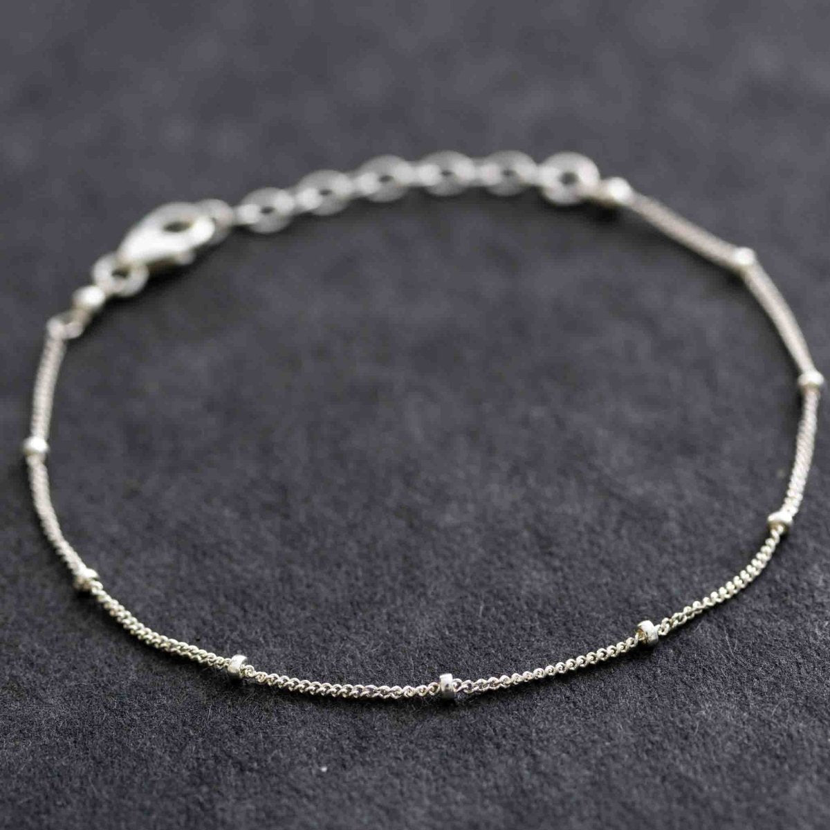 Feines Satelliten-Armband aus 925 Silber auf dunkelgrauem Hintergrund.