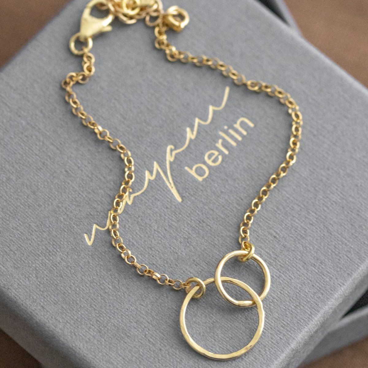 Vergoldetes 925 Silber-Armband mit zwei verschlungenen und gehämmerten Ringen auf grauem Schmucketui mit eingeprägtem Namen Mayam Berlin.