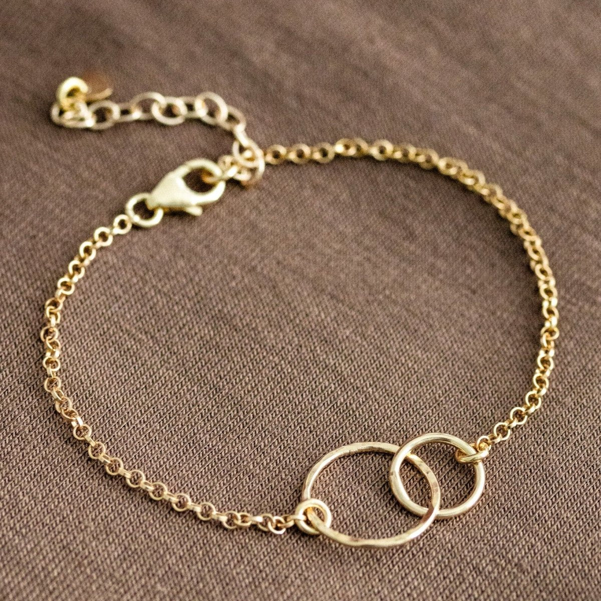 Vergoldetes 925 Silber-Armband mit zwei verschlungenen und gehämmerten Ringen auf braunem Hintergrund.