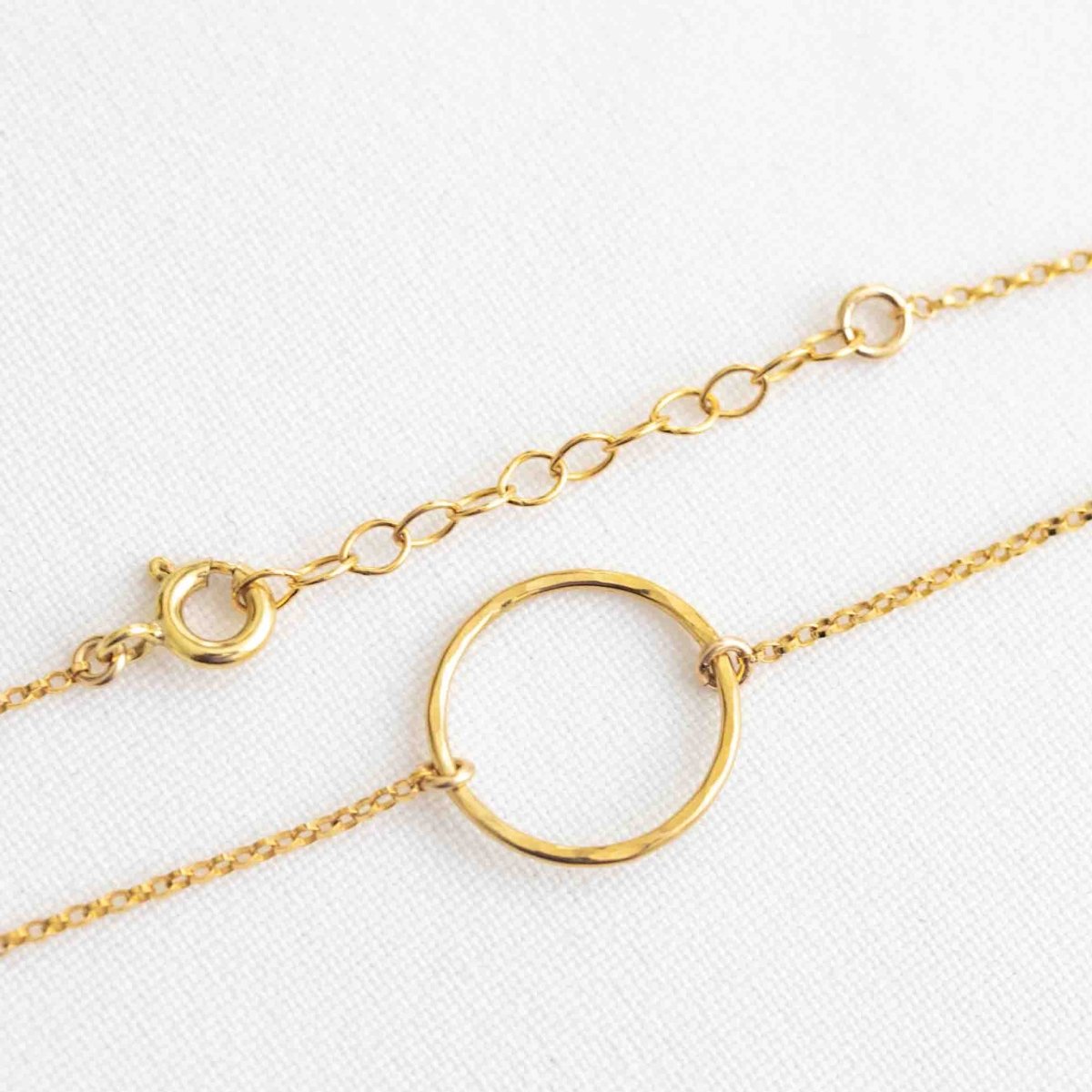 Ein goldenes Armband mit offenem Ring in der Mitte und Verschluss mit Federring und Verlängerungskettchen liegt auf weißem Hintergrund.