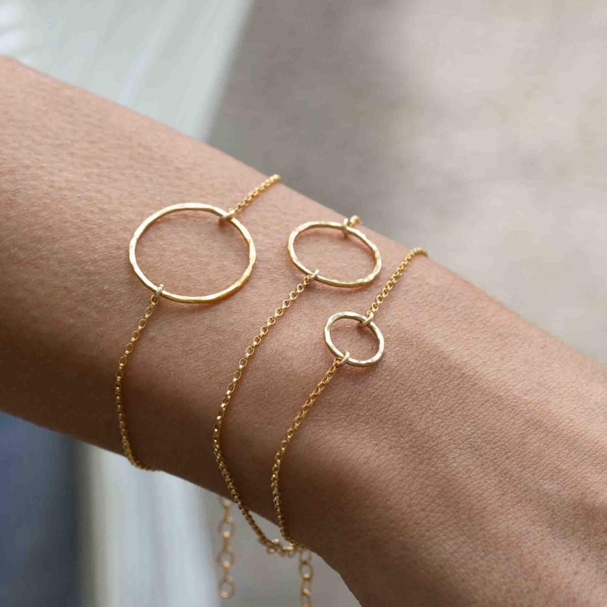 Das Model trägt am Handgelenk drei goldene Armbänder. Jedes Armband hat einen offenen Ring in der Mitte, jeweils unterschiedlicher Größe.