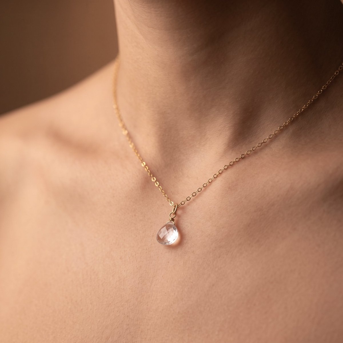 Feine Goldkette mit Bergkristall-Tropfen am Hals getragen.