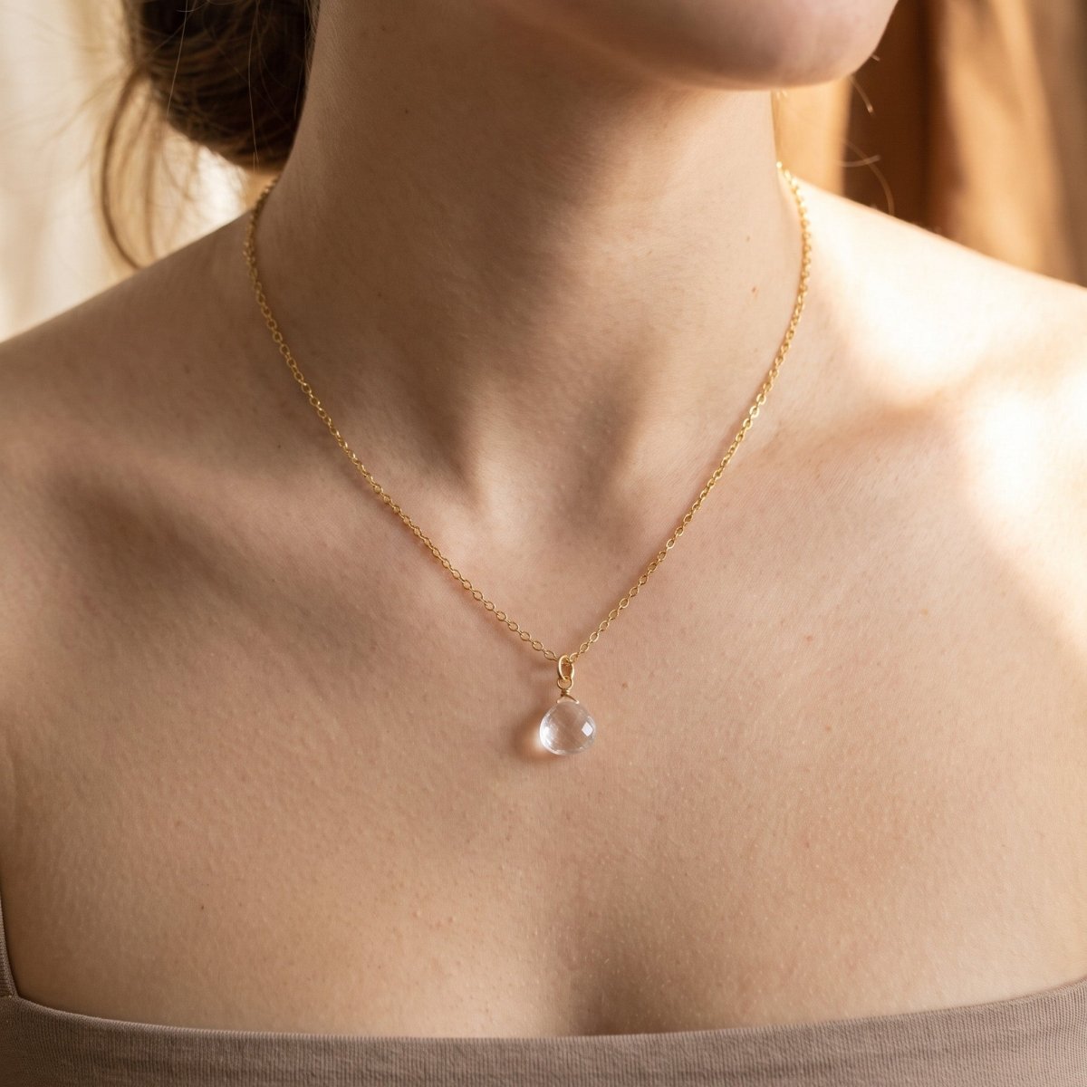 Feine Goldkette mit Bergkristall-Tropfen am Hals getragen.