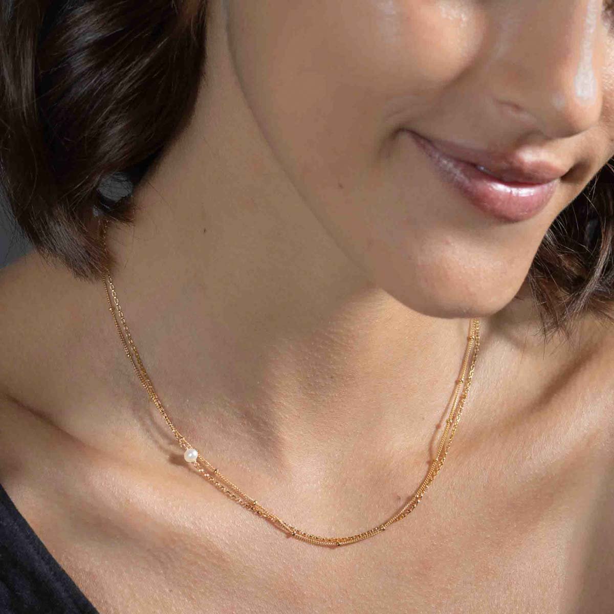 Eine feine, doppelreihige Goldkette mit einer kleinen Süßwasserperle am Hals des Models.